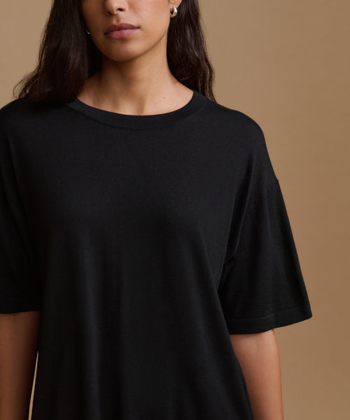 A close-up of a model wearing a black short-sleeve crewneck t-shirt against a solid warm brown background.
