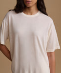 A close-up of a model wearing a cream-colored, oversized short-sleeve crewneck t-shirt against a solid beige background.