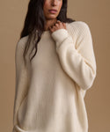 A woman wearing a cream-colored ribbed knit sweater against a solid beige background.