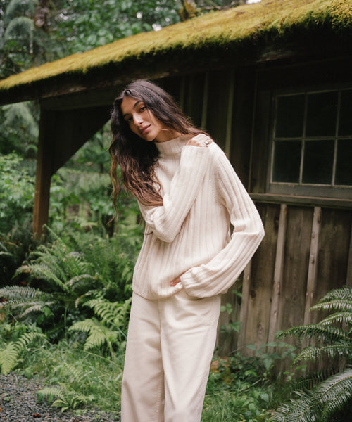 A woman standing outside wearing an ivory sweater with cream jeans. 