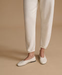 A person wearing cream-colored jogger pants and matching flat ballet flats, standing against a solid beige studio background.