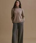 A model wearing high-waisted, wide-leg trousers with vertical brown, beige, and gray stripes, paired with a brown long-sleeve top.