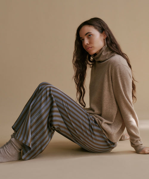 A model wearing high-waisted, wide-leg trousers with vertical brown, beige, and gray stripes, paired with a brown long-sleeve top.