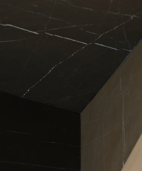 A close up of a rectangular black marble coffee table with white veining, set against a solid warm beige background.