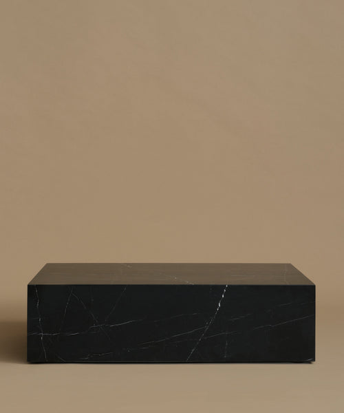 A rectangular black marble coffee table with white veining, set against a solid warm beige background.