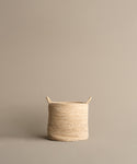 The Woven Storage Basket, featuring two small handles, rests on a neutral beige background. Its light color and stylish design make it an ideal solution for home storage needs.