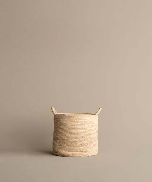 The Woven Storage Basket, featuring two small handles, rests on a neutral beige background. Its light color and stylish design make it an ideal solution for home storage needs.