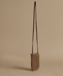 A small shoulder bag with a textured taupe-brown body and a dark brown leather strap, standing upright against a solid beige background.