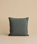 A dark gray Adler Pillow is centered against a beige background, showcasing its smooth Belgian linen cover. The luxury pillow appears plump and soft, highlighting its simple yet elegant design.
