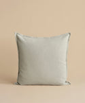 The Adler Pillow, featuring a square shape and light gray hue in a premium linen blend, stands upright against a simple beige background.