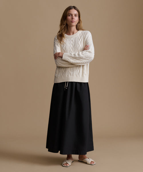 Woman wearing a cream cable knit sweater and black skirt on a beige background
