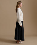 Woman wearing a white cable knit sweater and black skirt on a beige background