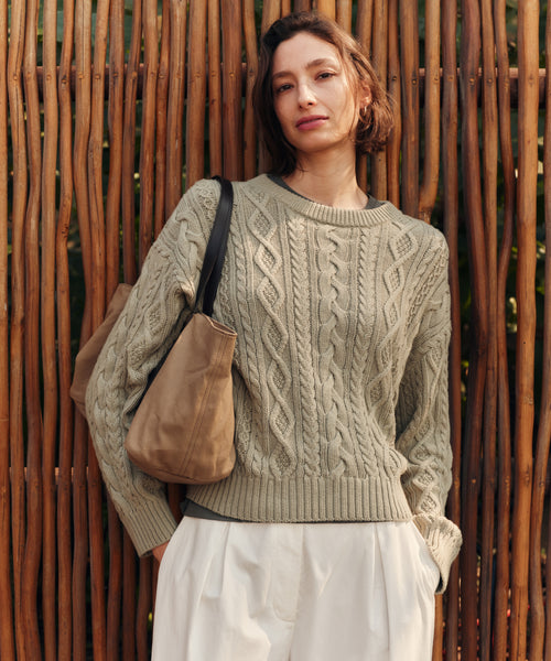 Woman wearing a cable knit sweater against a wooden fence