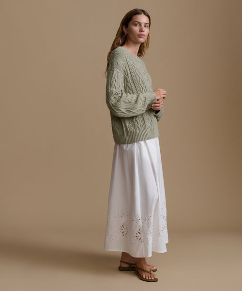 Woman wearing a green sweater and white dress against a beige background