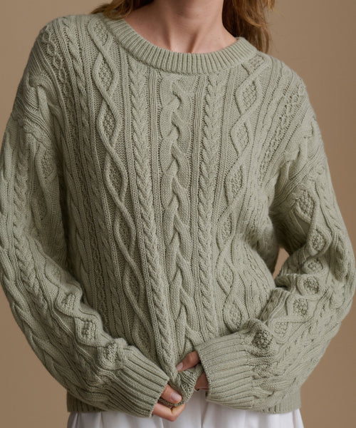 Green cable knit sweater worn by a person on a beige background