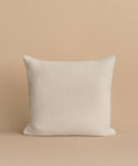 The Alpaca Basketweave Pillow, a square white accent, is handmade in Peru and sits upright on a beige surface with a matching beige background for an elegant touch.
