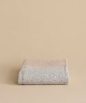 The Alpaca Colorblock Throw, handmade in Peru in soft beige and light grey, is neatly folded and displayed on a matching beige background.