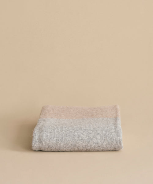 The Alpaca Colorblock Throw, handmade in Peru in soft beige and light grey, is neatly folded and displayed on a matching beige background.