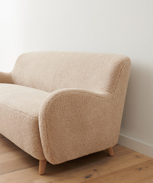 The Aspen Sofa features rounded arms and wooden legs, upholstered in cozy Oatmeal Sherpa for a mid-century modern look, making it an elegant addition to any room.