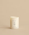 A white Basil Glass Candle labeled jenni kayne sits on a beige surface. Hand-poured in Los Angeles, it features notes of neroli, green herbs, and jasmine—a blend from Oprah’s Favorite Things.