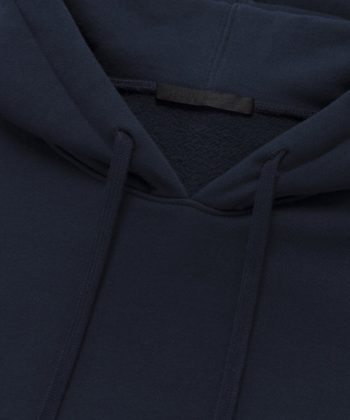 Close-up of the Bay Hoodie in dark navy blue, made from soft brushed fleece, highlighting the hood, drawstrings, collar, and a blank black tag.