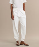 A person wearing a white t-shirt and Bay Sweatpant joggers, crafted from brushed fleece with an elastic waistband and drawstring, stands in sandals against a neutral background. The persons head is not shown.