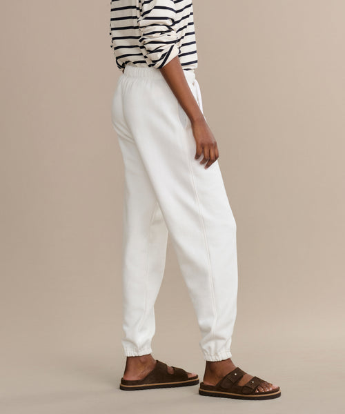 Wearing a black-and-white striped long-sleeve shirt, Bay Sweatpant in brushed fleece, and brown sandals, a person stands sideways against a beige background with their left arm relaxed by their side.