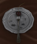 A dark cherry on a fork rests on a vintage metal plate, surrounded by Small Loren Pearl Studs and silver necklaces, all set against a rich brown fabric background.