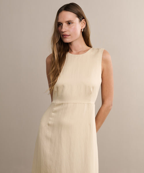 A woman with long, straight brown hair wears the sleeveless, light beige Blair Dress, paired with small earrings. She stands against a plain, light background, looking slightly to her left—an ideal choice for your spring wardrobe.