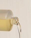 A close-up of a glass bottle pouring light yellow liquid against a plain background—perfect for highlighting the radiance and hydration benefits of Body Hydration Heroes.