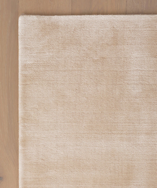 A close-up of the Bristol Rug’s beige, textured handwoven corner on a light wooden floor, handmade in India.
