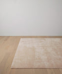 The Bristol Rug, a large handwoven piece in light pink with a soft texture, is placed on a light wooden floor in a minimalistic room with white walls.