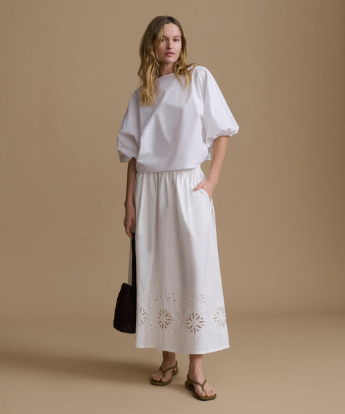 Woman wearing a white top and skirt with cut-out details on a beige background