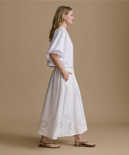 Woman wearing a white top and skirt with cut-out details on a beige background