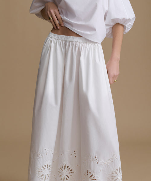 White blouse and skirt with intricate cut-out design on a beige background