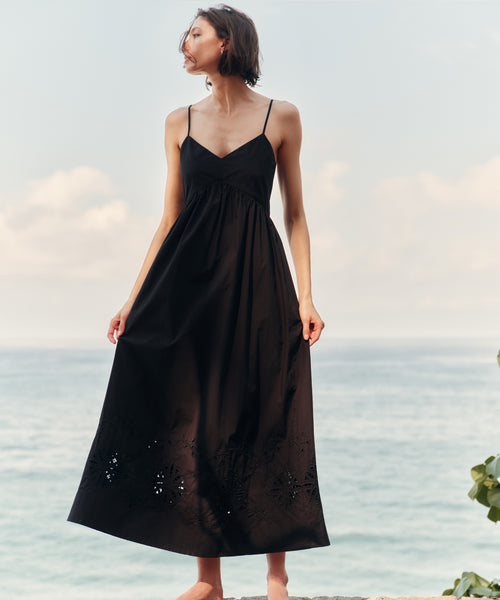 Woman in a black dress standing by the ocean with a soft sky background