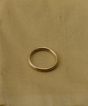 The Brook Gold Band, crafted in 14k gold, is displayed on a light tan fabric background with a subtle texture and minor stains.