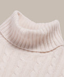 Close-up of the Cable Nell Turtleneck in ivory, showcasing its ribbed collar and textured cable knit pattern against a plain backdrop.