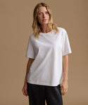 A woman modeling a plain white short-sleeve crewneck t-shirt against a solid warm beige studio background.