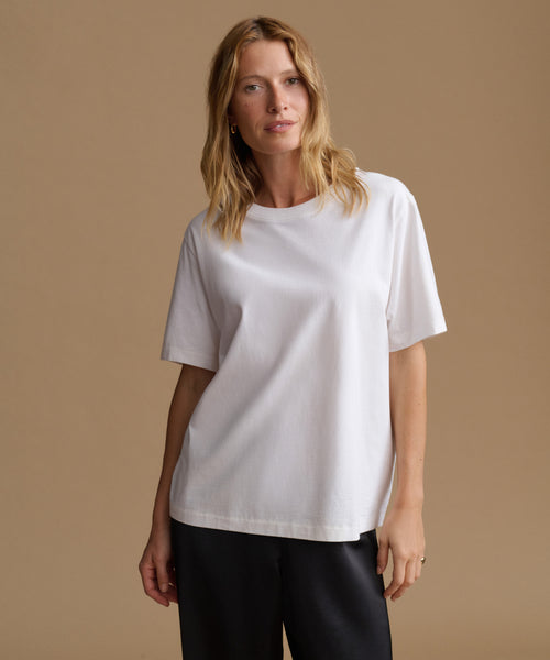 A woman modeling a plain white short-sleeve crewneck t-shirt against a solid warm beige studio background.