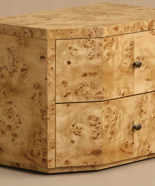 A close-up of the Carbon Nightstand highlights its light wood grain and two drawers with round metal knobs, giving it a modern look.