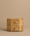 The Carbon Nightstand is a compact, lightweight piece featuring a natural burled wood grain, two drawers with round metal knobs, and a modern design, displayed against a plain beige background.