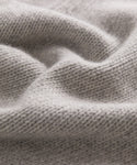 Close-up of soft, light gray knit fabric with a wavy texture and visible stitches, capturing the warmth and coziness of the Cashmere Amelia Crewneck sweater.
