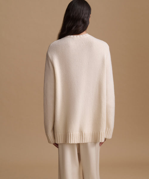 A model shown from the back wearing a cream-colored knit sweater and matching trousers against a solid beige background.