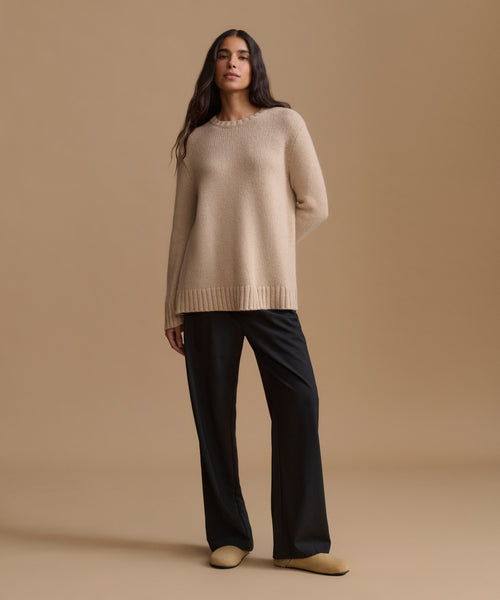 A woman modeling a beige knit sweater  with black wide-leg trousers and beige flats, set against a solid beige studio background.