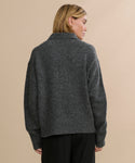 A person with short blonde hair, seen from behind, is wearing a Cashmere Burke Polo in dark gray with black pants against a plain, light beige background.