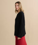 A woman with shoulder-length blonde hair stands sideways against a plain beige background, wearing the Cashmere Chandler Long-Sleeve Tee and a red skirt.