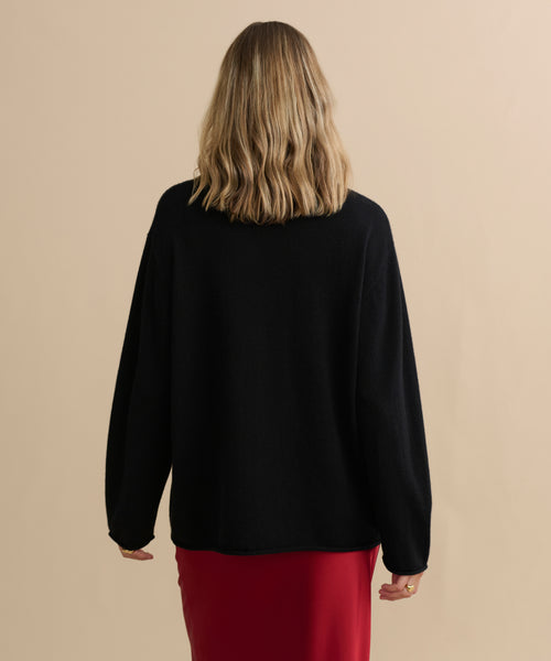 A person with shoulder-length wavy blonde hair is shown from behind, wearing the Cashmere Chandler Long-Sleeve Tee and a red skirt, standing against a plain beige background.