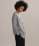 A woman with curly hair stands sideways in the Cashmere Cocoon Cardigan and black pants, looking at the camera with a neutral expression against a plain background.