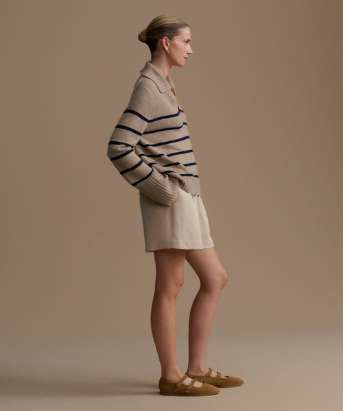 Woman wearing a beige cashmere sweater with black stripes and a beige skirt against a brown background